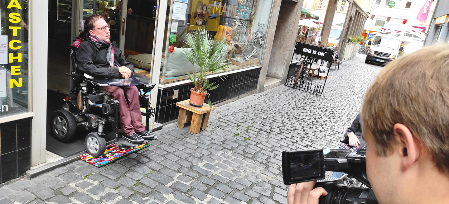 Julian Wendel testet mit seinem E-Stuhl unsere erste ausgelegte Legorampen vor dem Café Maincake in der Würzburger Altstadt.
